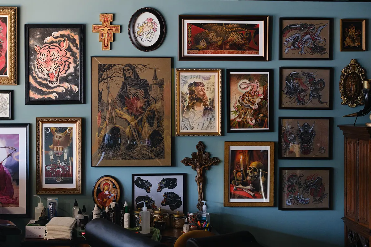 The gallery wall at Pilgrimage Tattoo: framed paintings, prints and tattoo flash above English's workstation