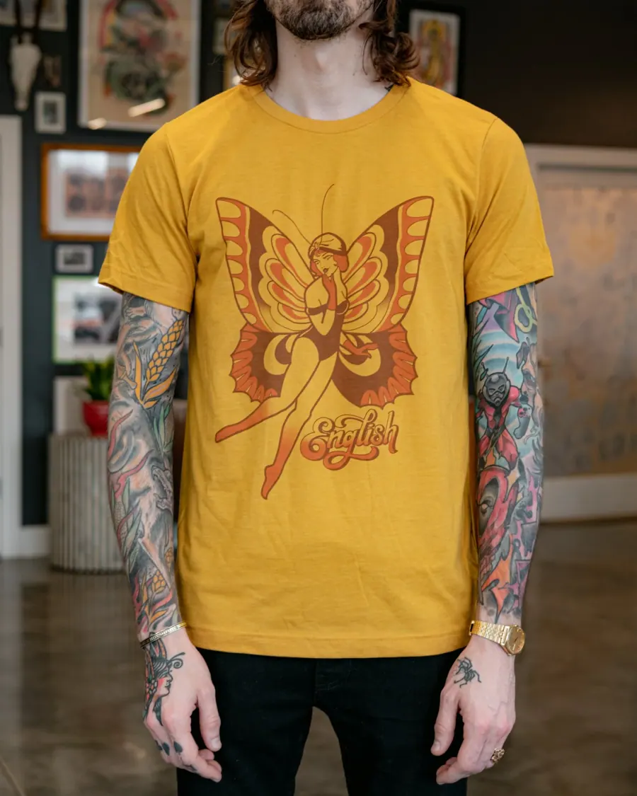 A person wearing a yellow T-shirt with a graphic of a woman with butterfly wings and the word English written below