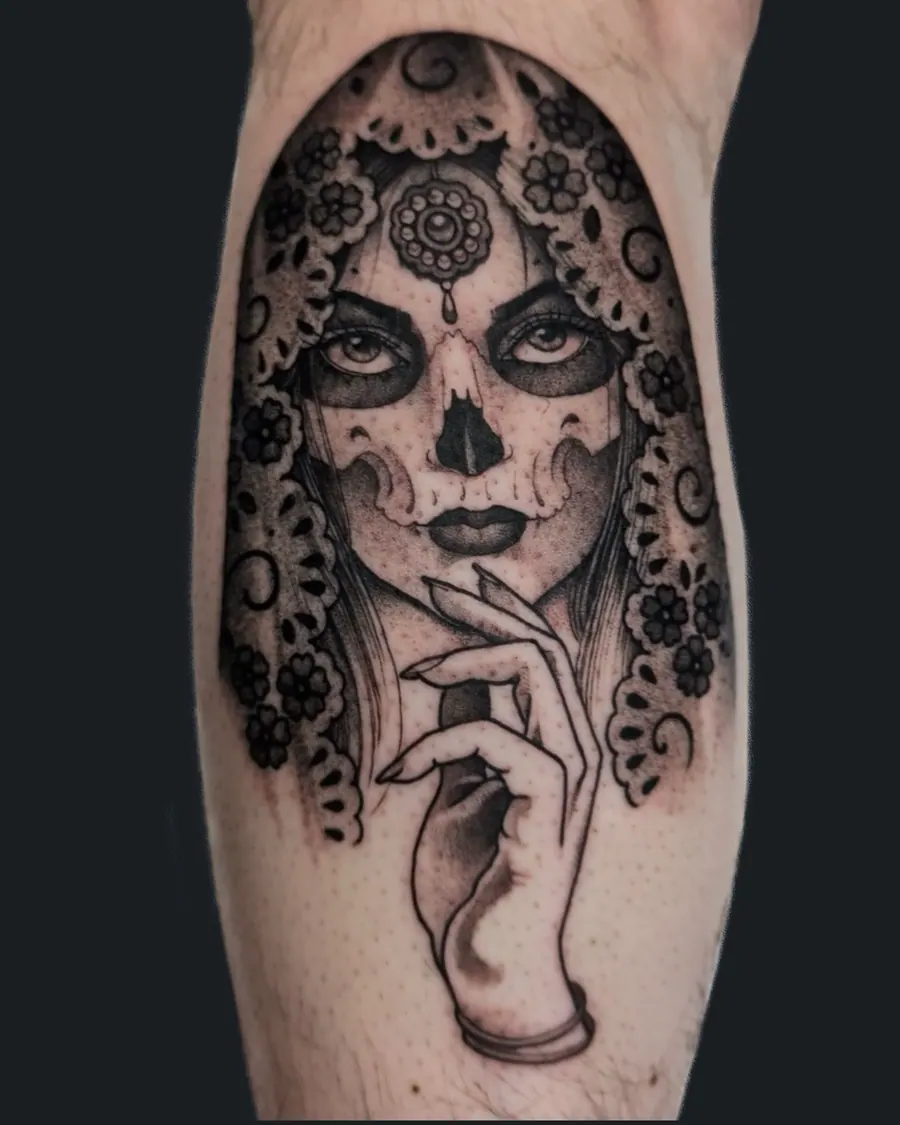 Black and gray tattoo of a woman in a lace mantilla veil with skull face paint, her hand resting on a crystal ball, on the calf by English Cousins, Nashville