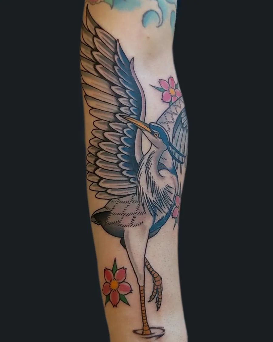Tattoo of a heron with outstretched wings surrounded by pink cherry blossoms on the arm by English Cousins, Nashville