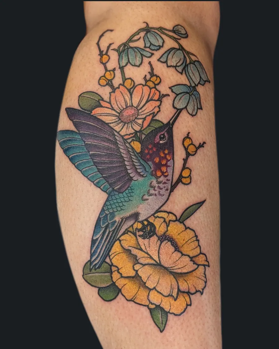 Colorful hummingbird tattoo hovering between a yellow peony, a cosmos and bluebells on the calf by English Cousins, Nashville