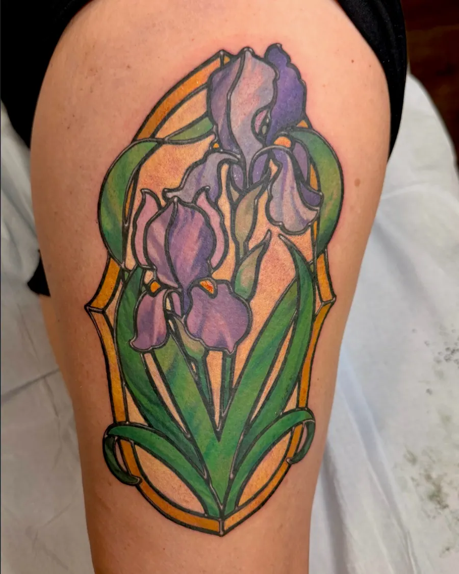 Art Nouveau purple iris tattoo set in a stained-glass frame with green leaves on the thigh by English Cousins, Nashville