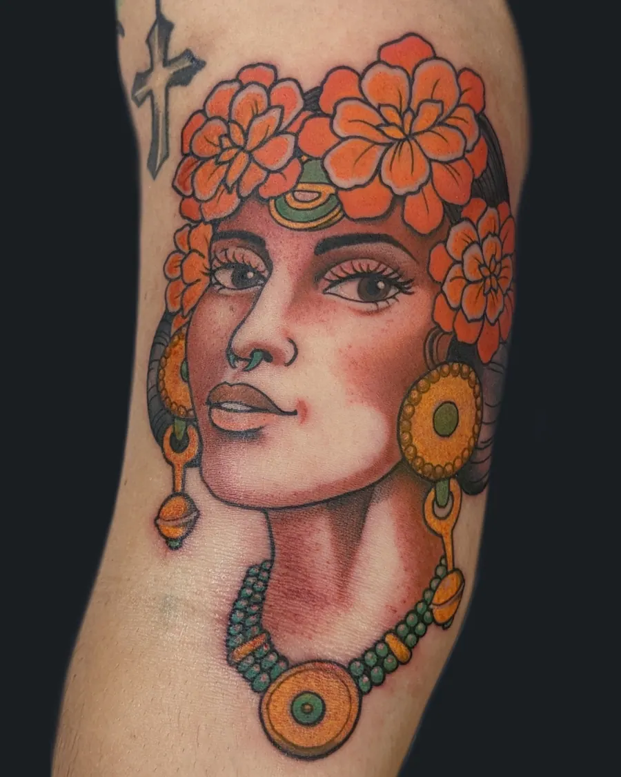 Colorful tattoo of a woman with large orange flowers in her hair, wearing large earrings, a nose ring, and a beaded necklace by English Cousins, Nashville