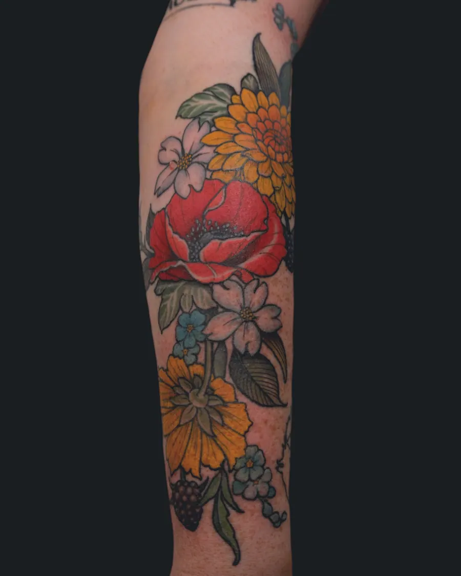 Colorful floral tattoo featuring a red poppy, yellow chrysanthemum, dogwood blossoms, blue forget-me-nots, and blackberries by English Cousins, Nashville