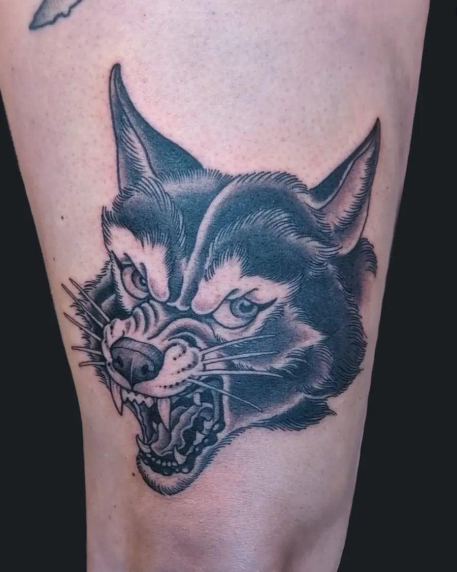 Black and gray tattoo of a snarling wolf's head on the thigh by English Cousins, Nashville