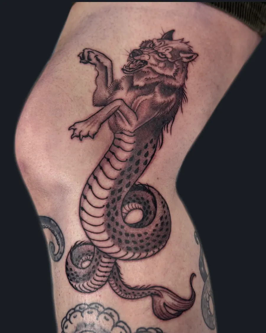 Black and gray tattoo of a wolf-headed serpent coiled over the knee by English Cousins, Nashville